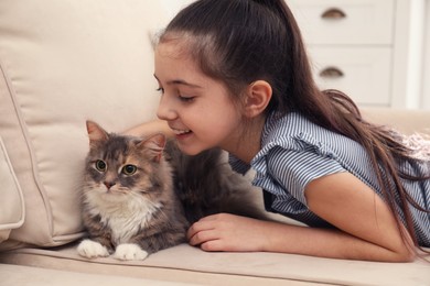 Photo of Cute little girl with cat on sofa at home. First pet