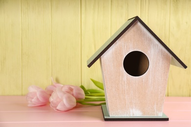Photo of Beautiful bird house and tulips on pink wooden table, space for text