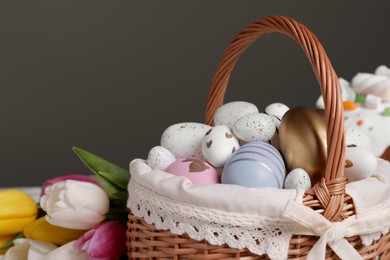 Wicker basket with festively decorated Easter eggs and beautiful tulips on dark grey background, closeup