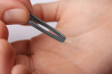 Photo of Woman pulling splinter from hand using tweezers on white background, closeup
