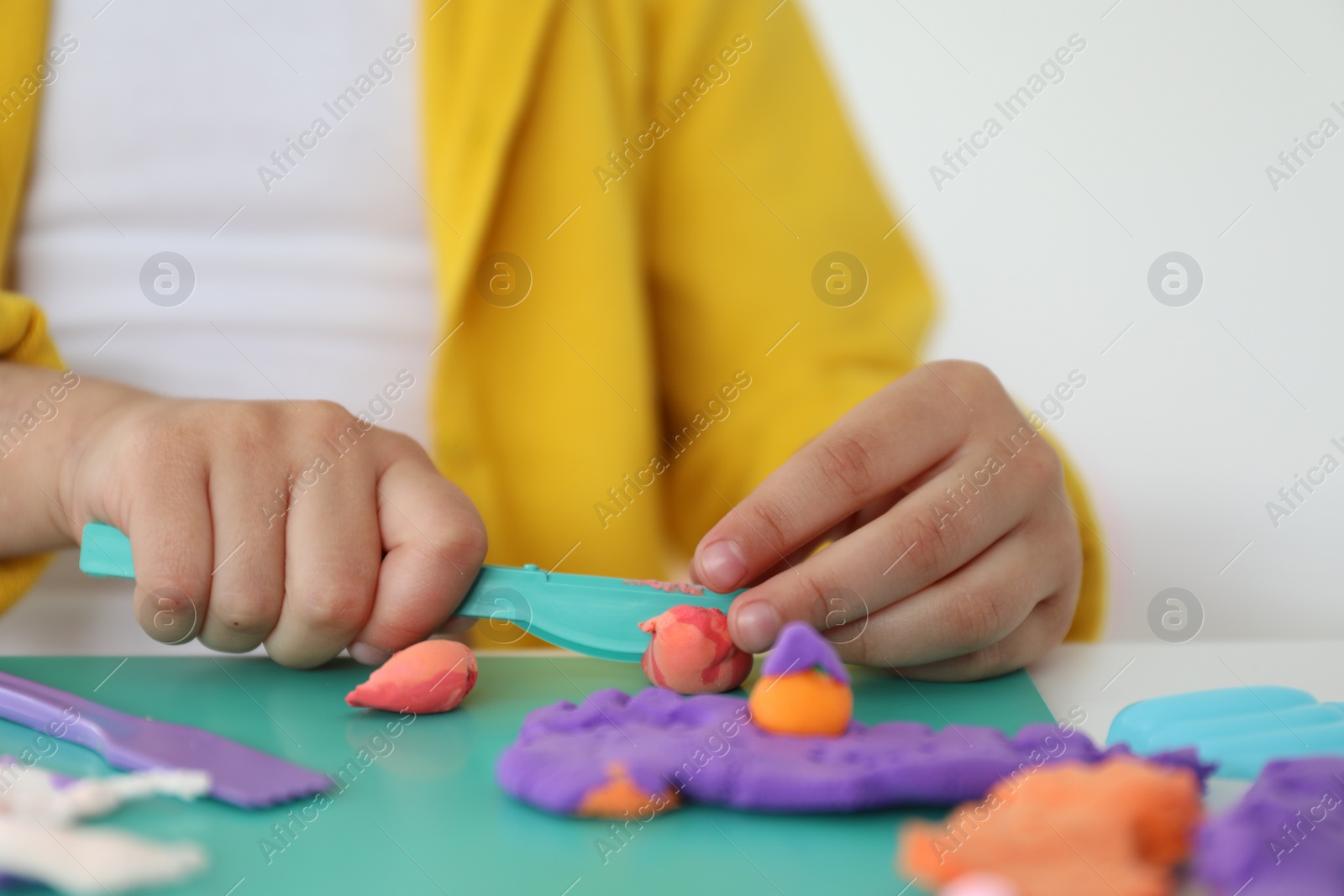 Photo of Little girl sculpting with play dough at table indoors, closeup