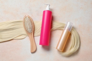 Photo of Spray bottles with thermal protection, lock of blonde hair and hairbrush on beige textured table, flat lay