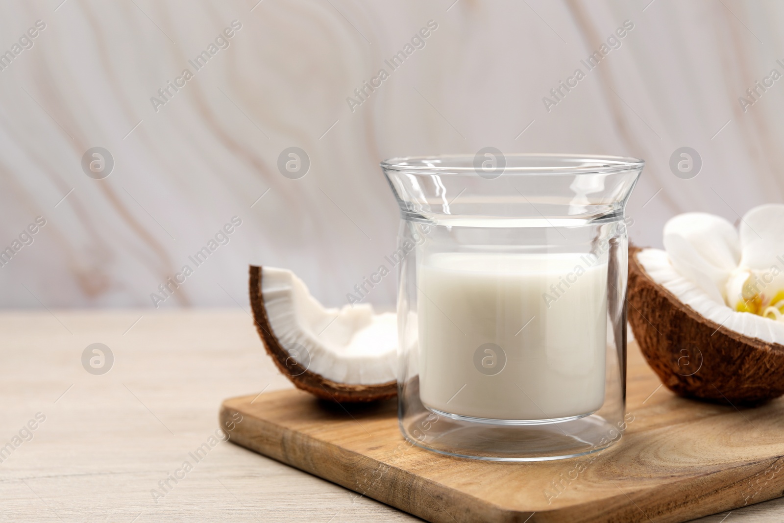 Photo of Glass of delicious vegan milk, coconut pieces and flower on white wooden table. Space for text