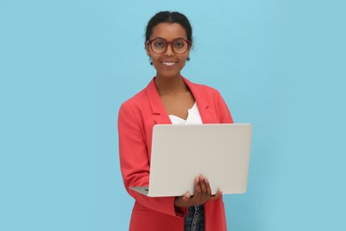 Photo of Smiling African American intern working on laptop against light blue background
