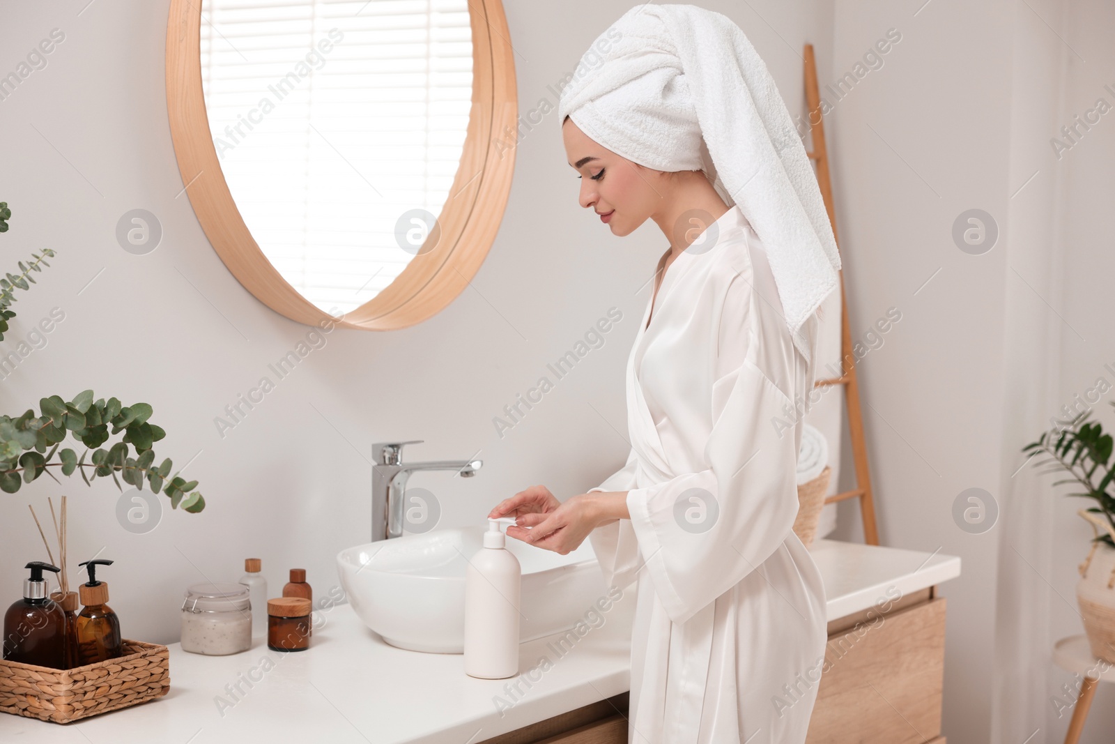 Photo of Beautiful young woman using body cream in bathroom, space for text