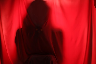 Silhouette of creepy ghost behind red cloth, space for text