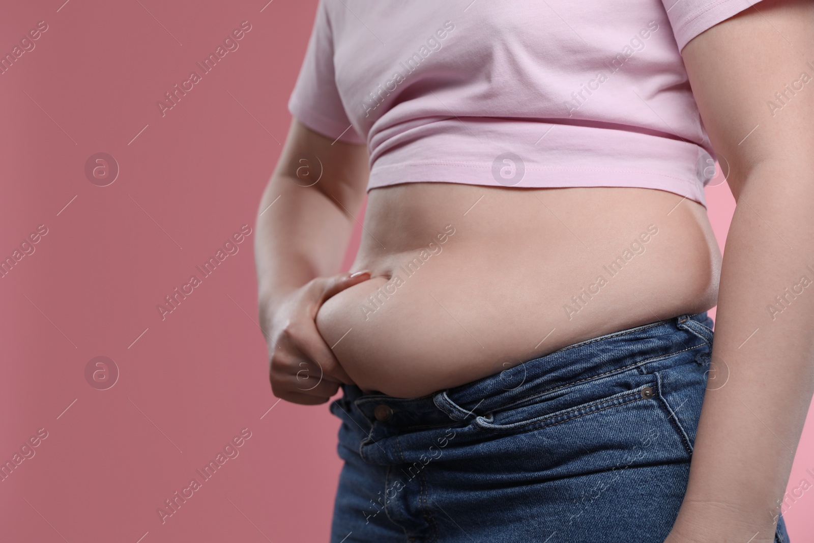 Photo of Woman touching belly fat on pink background, closeup. Overweight problem