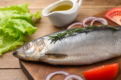 Board with delicious salted herring and ingredients on wooden table, closeup