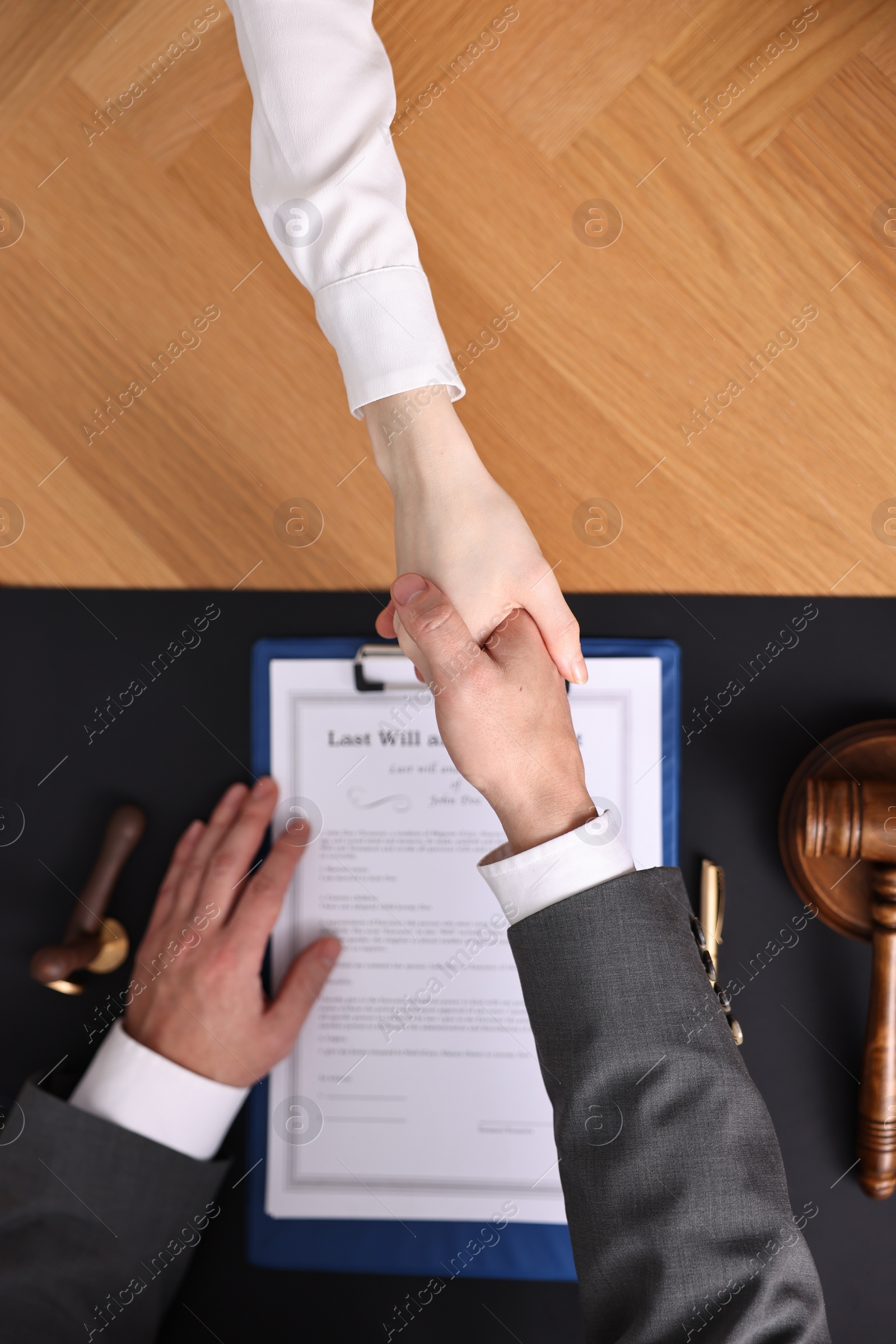 Photo of Notary shaking hands with client at wooden table, top view