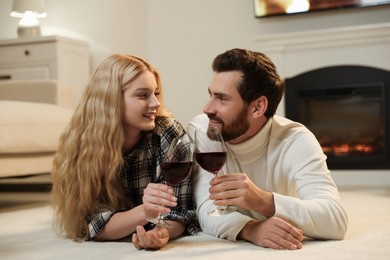 Lovely couple with glasses of wine spending time together near fireplace at home
