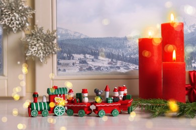 Image of Burning candles and toy train on white window sill indoors. Christmas eve
