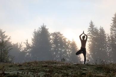 Woman practicing yoga in mountains at sunrise, back view