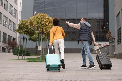 Photo of Being late. Man and woman with suitcases running outdoors, back view