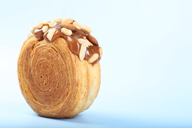 Photo of One supreme croissant with chocolate paste and nuts on light blue background, closeup with space for text. Tasty puff pastry