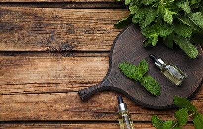 Bottles of essential oil and mint on wooden table, flat lay. Space for text