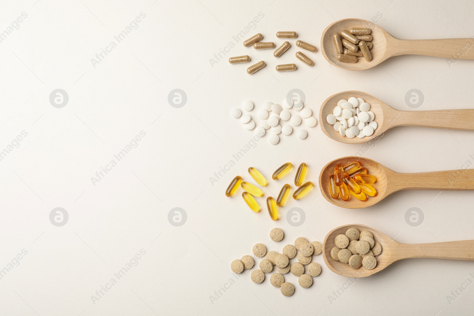 Photo of Wooden spoons and different dietary supplements on white background, flat lay. Space for text