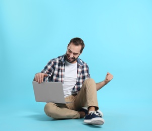 Photo of Emotional young man with laptop celebrating victory on color background