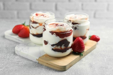 Photo of Tasty yoghurt with jam and strawberries on grey table, closeup