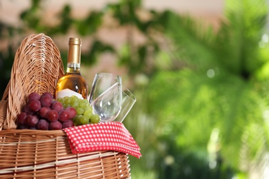 Picnic basket with wine, glasses and grapes on blurred background, space for text