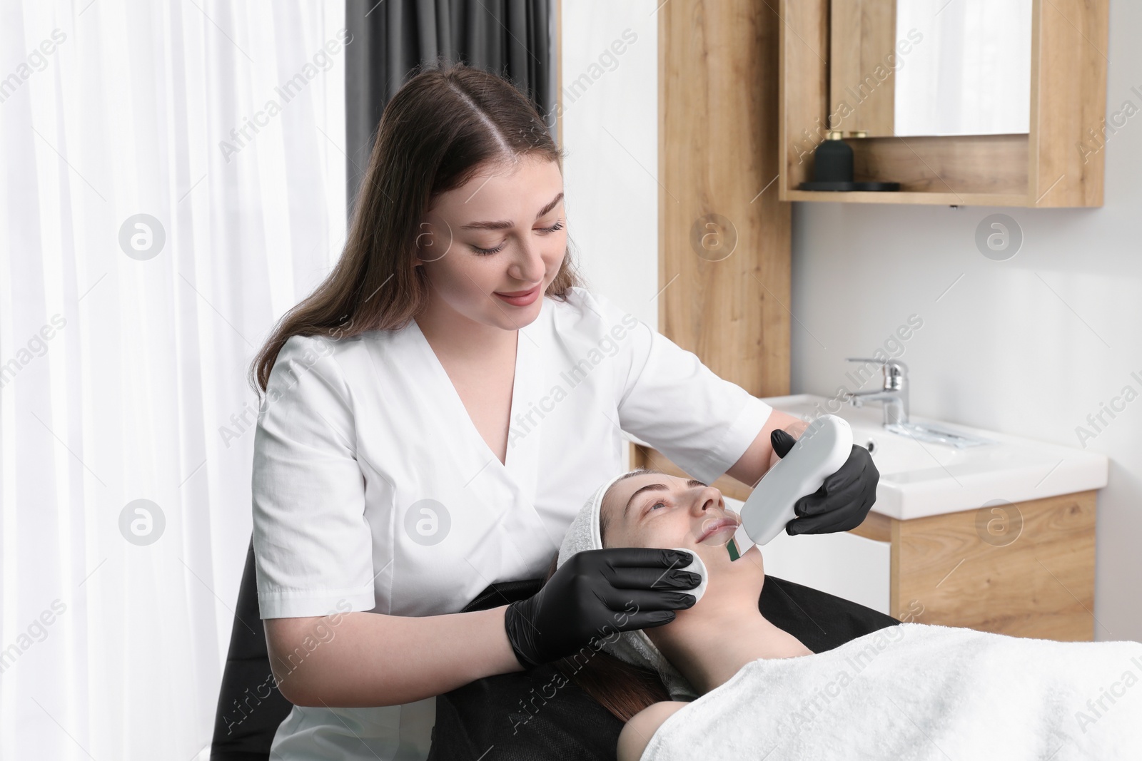 Photo of Cosmetologist using ultrasonic scrubber. Client having cleansing procedure in clinic