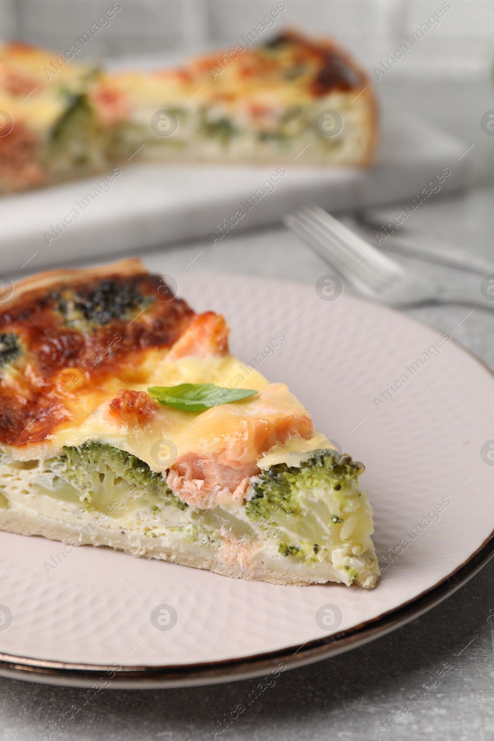 Photo of Piece of delicious homemade quiche with salmon and broccoli on light grey table, closeup