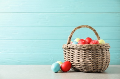 Photo of Wicker basket with colorful painted Easter eggs on table against wooden background, space for text