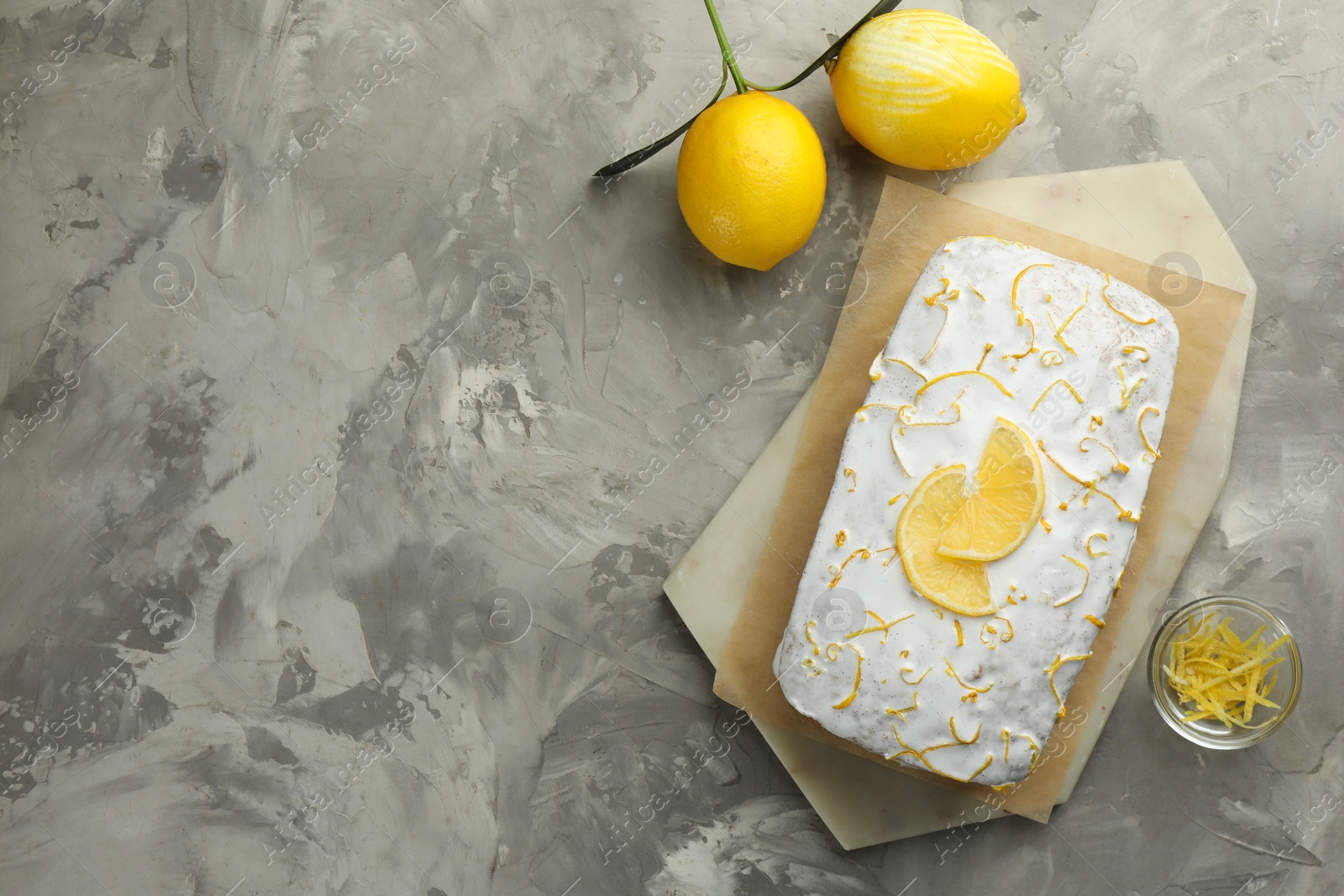 Photo of Tasty lemon cake with glaze, citrus fruits and zest on gray textured table, flat lay. Space for text