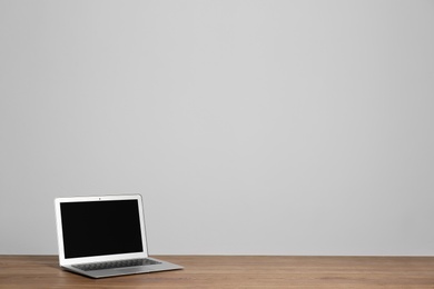 Modern laptop with blank screen on wooden table against gray background