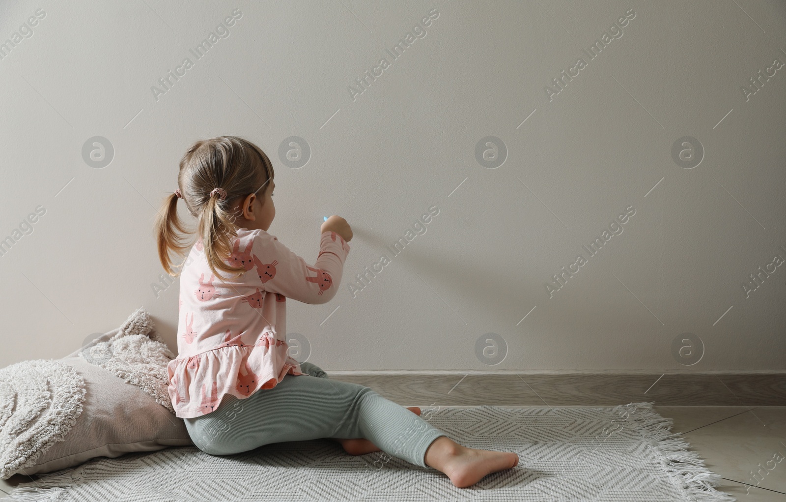 Photo of Little girl drawing on beige wall indoors, space for text. Child`s art