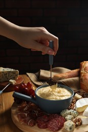 Photo of Woman dipping piece of bread into fondue pot with melted cheese at wooden table, closeup