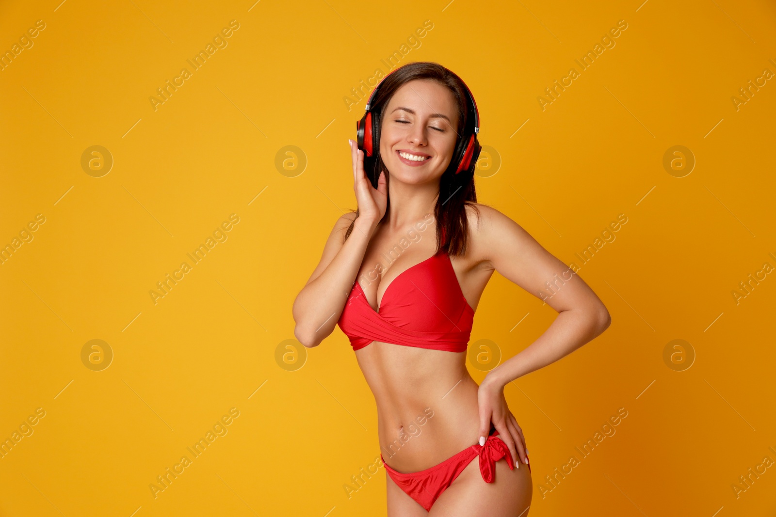 Photo of Pretty sexy woman with slim body in stylish red bikini and headphones on orange background, space for text