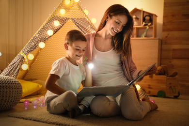 Photo of Mother and son with flashlight reading book at home