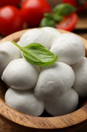 Photo of Delicious mozzarella balls and basil in bowl on wooden table, closeup