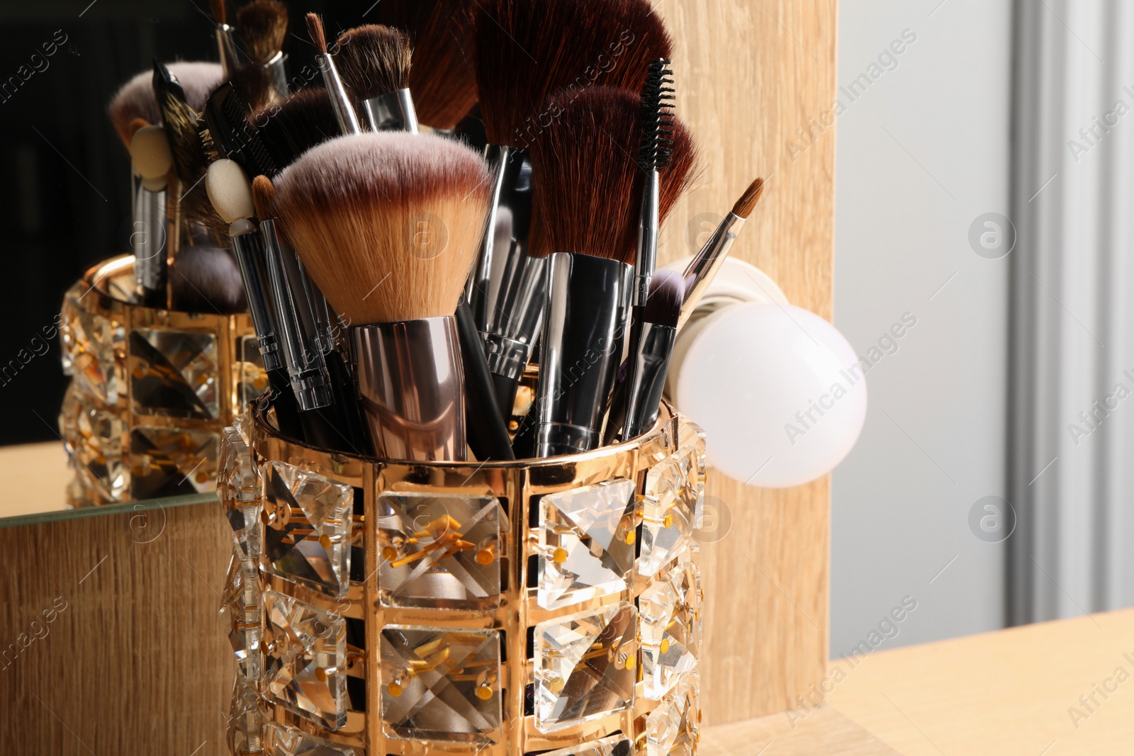 Photo of Set of professional makeup brushes near mirror on wooden table, closeup