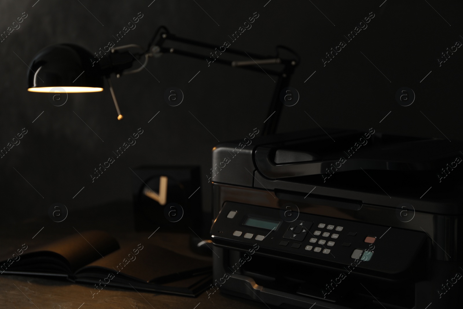 Photo of New modern printer, notebook and lamp on wooden table at night