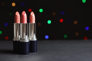 Photo of Different lipsticks on table against blurred lights. Space for text