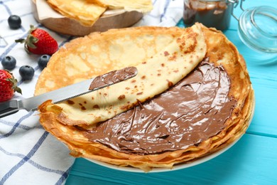 Photo of Tasty crepes with chocolate paste and berries served on turquoise wooden table, closeup