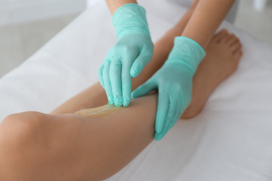 Photo of Woman getting wax epilation of legs in salon, closeup