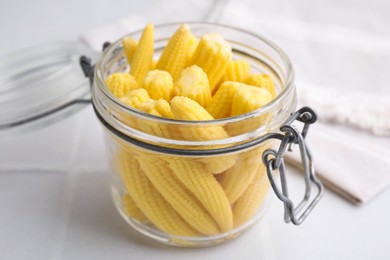 Photo of Tasty fresh yellow baby corns in glass jar on white tiled table, closeup