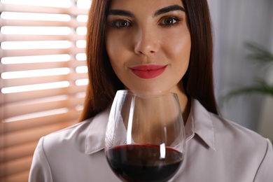 Photo of Beautiful young woman with glass of luxury red wine indoors, closeup view