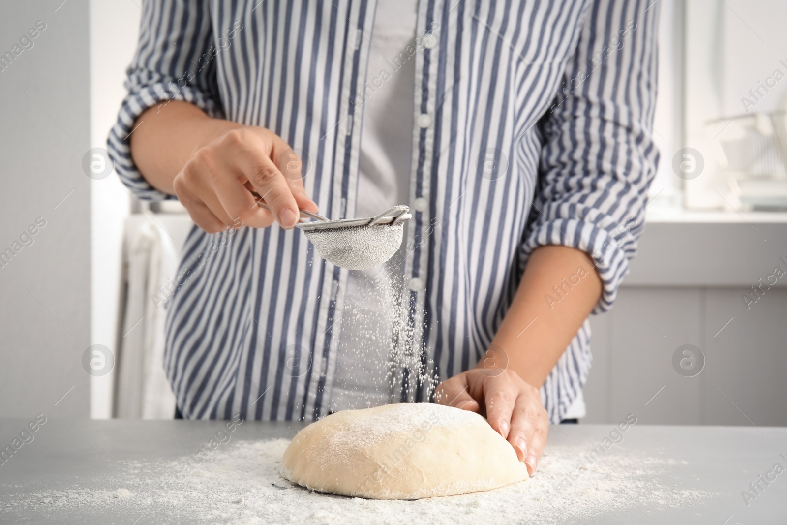 Photo of Woman sprinkling dough for pastry with flour on table