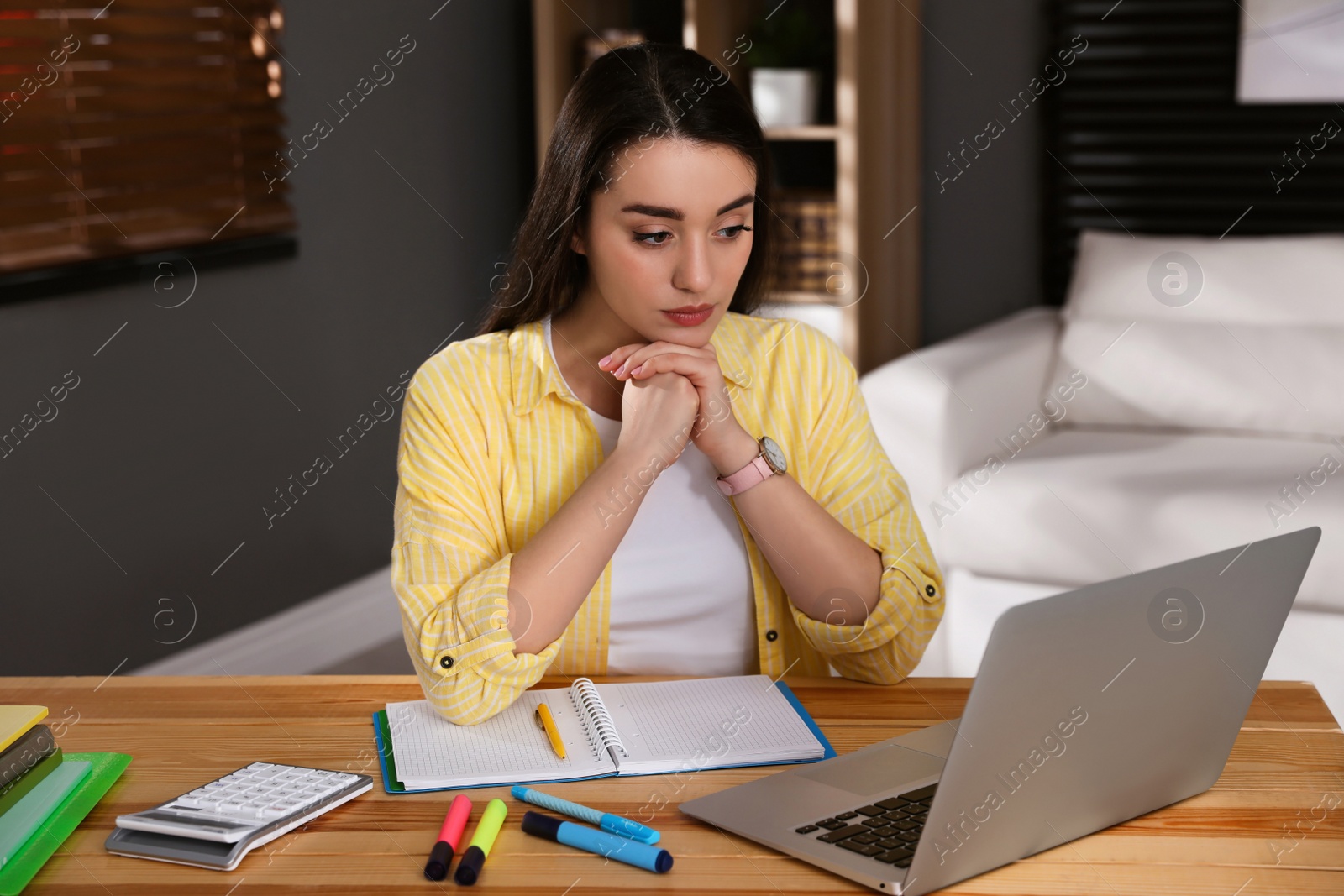 Photo of Young woman watching webinar at table in room