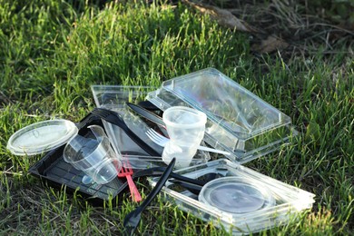 Photo of Used plastic tableware on grass outdoors. Environmental pollution concept