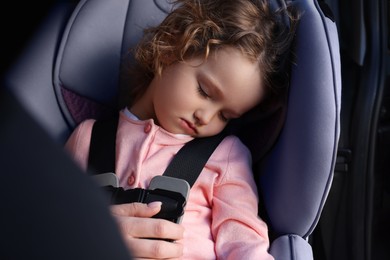 Photo of Cute little girl sleeping in child safety seat inside car