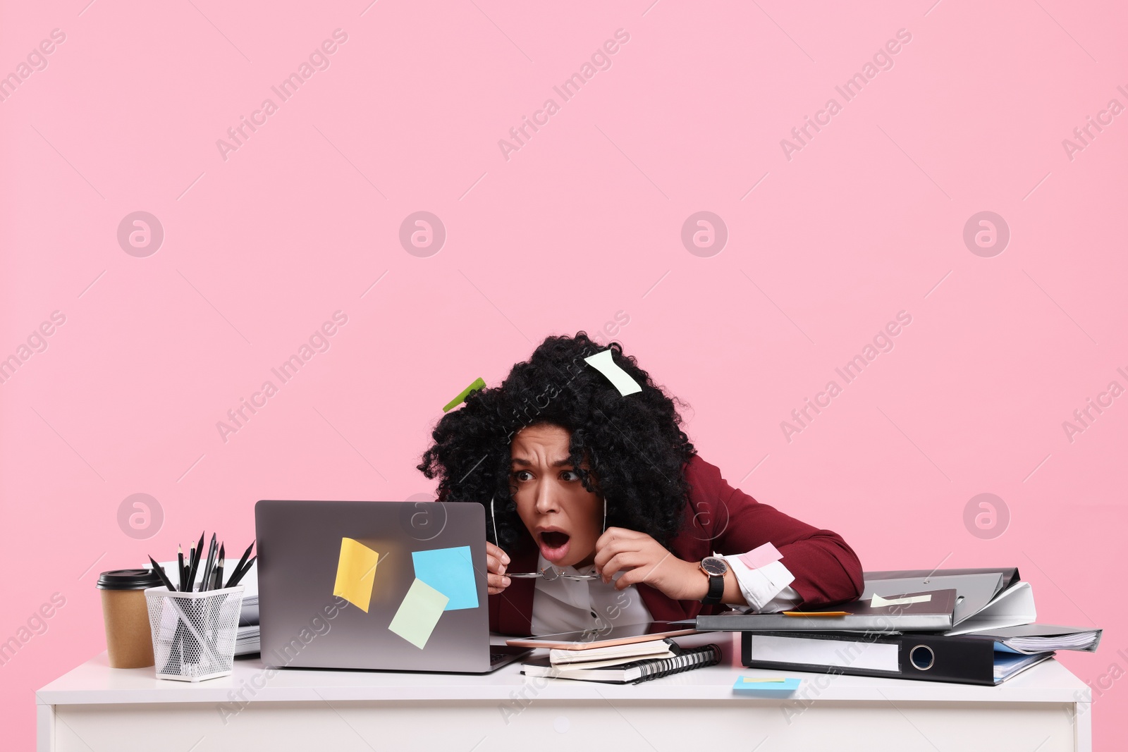 Photo of Stressful deadline. Scared woman looking at laptop at white desk on pink background, space for text. Sticky notes everywhere as reminders