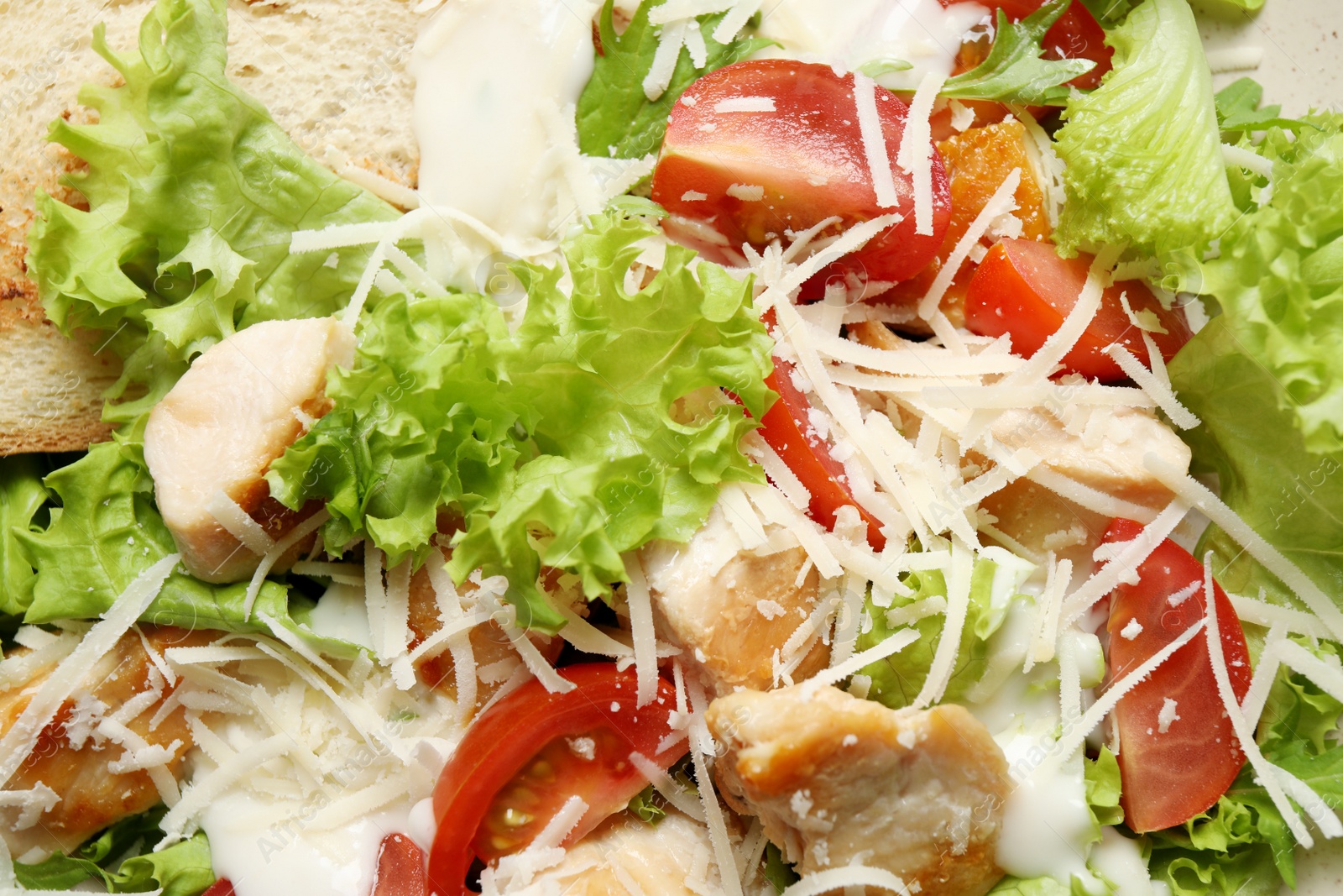 Photo of Delicious Caesar salad with fresh ingredients as background, closeup