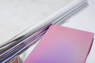 Photo of Beautiful notebook and rolled glossy wrapping paper on table