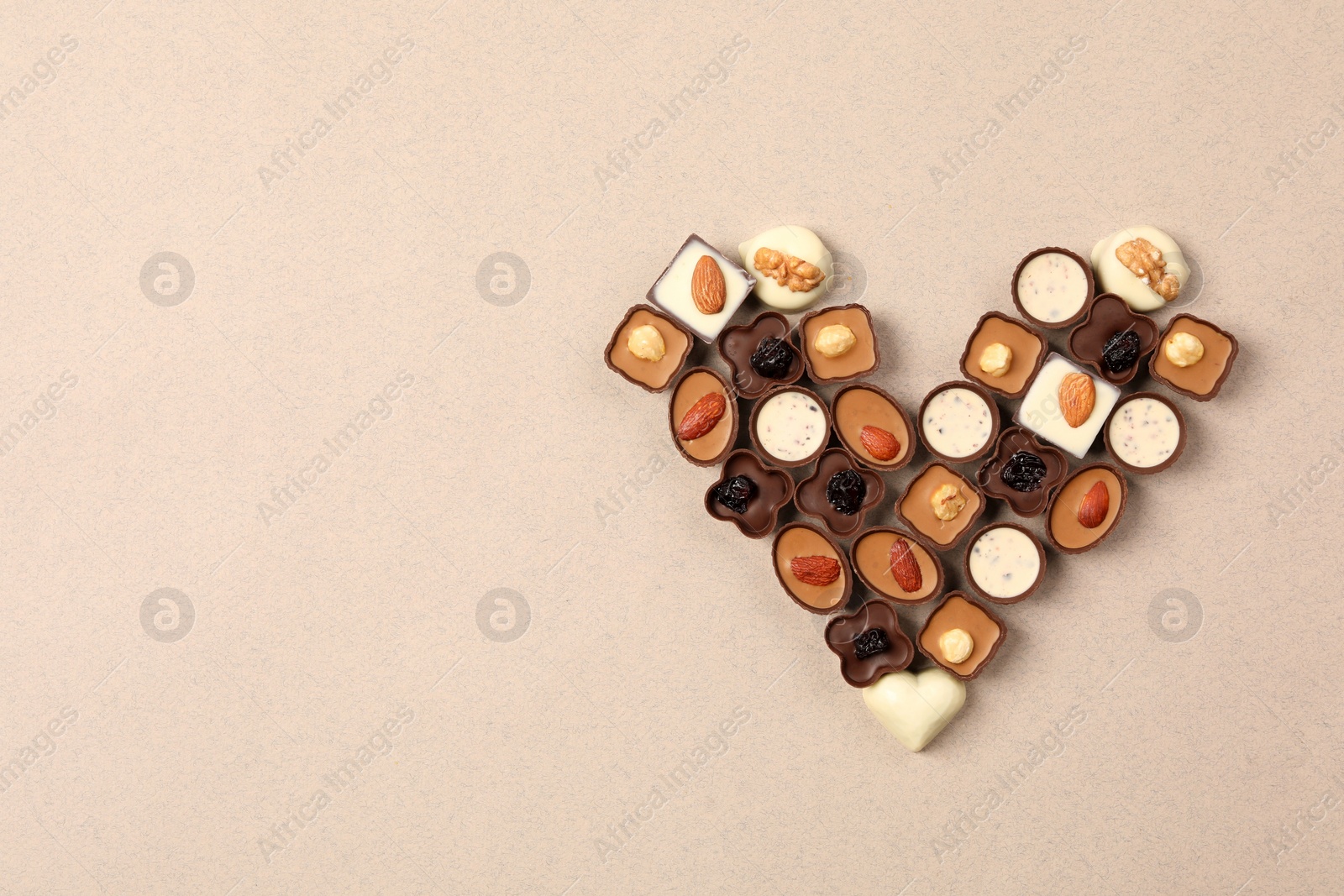 Photo of Heart made with delicious chocolate candies on beige background, top view. Space for text