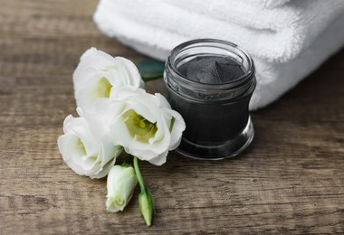 Folded towels, jar of cosmetic mask and eustoma flowers on wooden table