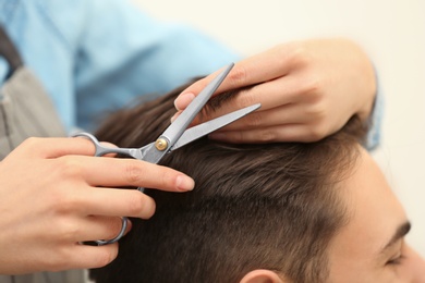 Photo of Barber making stylish haircut with professional scissors in beauty salon, closeup